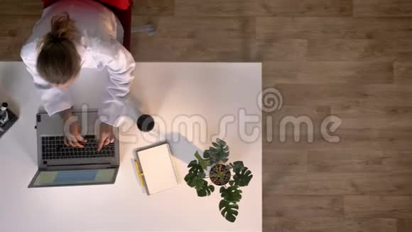 年轻的女科学家穿着白大褂在显微镜里看着在笔记本电脑上打字上面的照片医学实验室视频的预览图