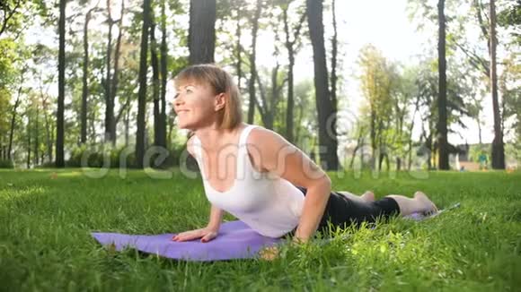 中年妇女在公园锻炼的4K镜头成年女性在森林里的fitnes垫子上练习瑜伽视频的预览图
