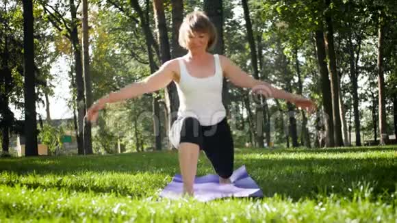 中年妇女在公园锻炼的4K镜头成年女性在森林里的fitnes垫子上练习瑜伽视频的预览图