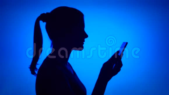 蓝色背景下使用手机的女人剪影女性的侧脸浏览聊天视频的预览图