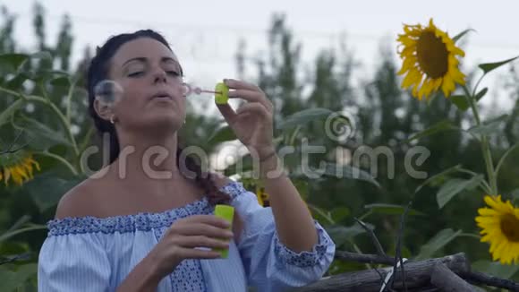 近景美丽的村妇与硬币释放肥皂泡在成长中的向日葵背景视频的预览图