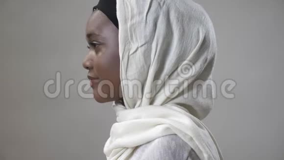 戴头巾的年轻非洲穆斯林女孩正转过头看着镜头微笑着宗教概念灰色背景视频的预览图