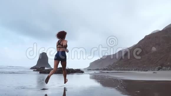 运动女性在海滩上奔跑黑色的沙子在山脉和海洋的背景下缓慢运动加那利视频的预览图
