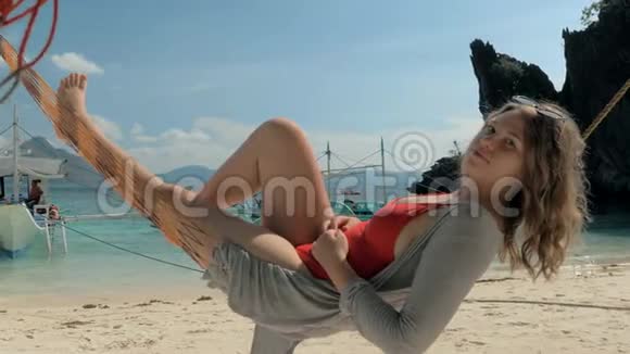 在炎热的夏日里快乐的年轻女子躺在热带沙滩上的吊床上休息视频的预览图