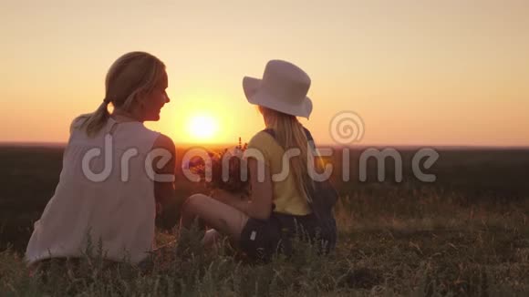 妈妈和小女儿坐在山上欣赏日落在野花的手中有孩子的夏天视频的预览图