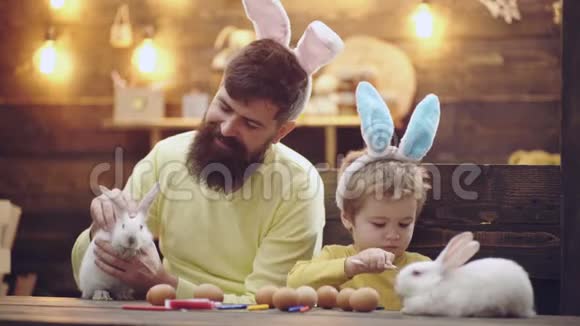幸福的家庭正在为复活节做准备可爱的小男孩戴着兔子耳朵一个男人和一个男孩把复活节彩蛋涂在视频的预览图
