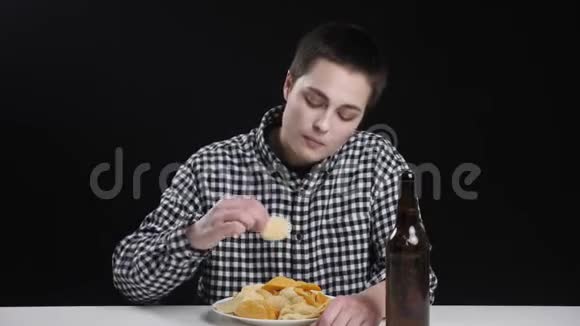 非凡的年轻女孩正在吃法国薯片桌上放着一瓶啤酒饮食观念黑色背景视频的预览图