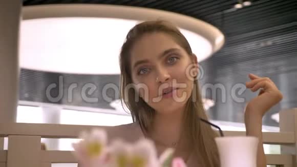 年轻漂亮的女孩坐在rastaurant里看着摄像机微笑着喝着咖啡放松概念做梦视频的预览图