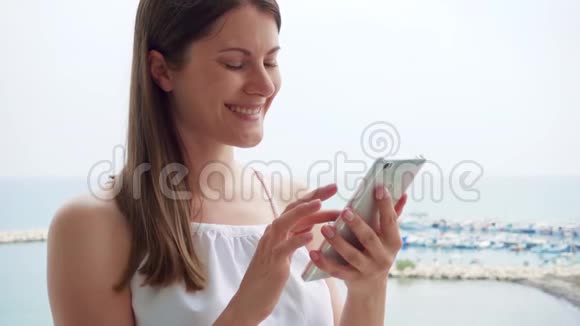女人在阳台上用手机女性在度假时通过手机慢动作与朋友聊天视频的预览图
