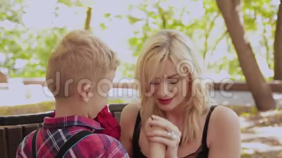 美丽的小男孩在公园里的长凳上给他心爱的母亲一束花视频的预览图