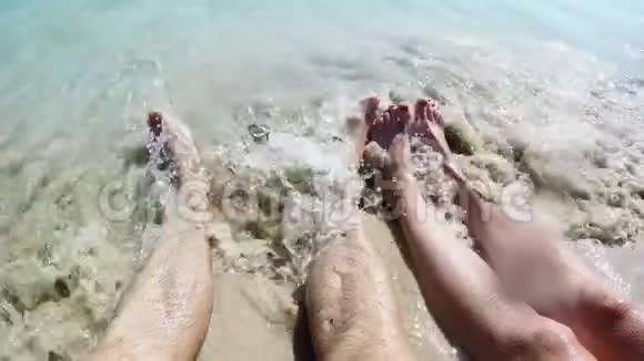 人们的脚被海浪冲刷然后埋在沙子里一对躺在沙滩上的男女脚的特写镜头视频的预览图