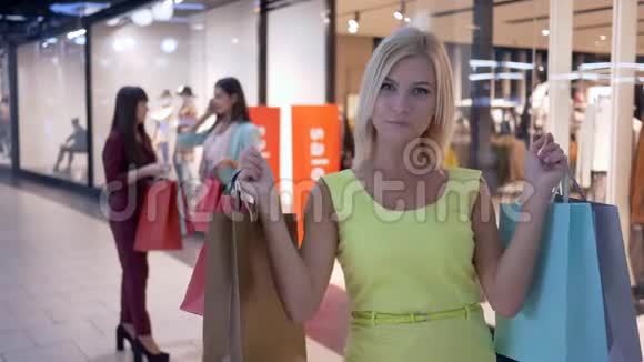 购物女孩穿着黄色衣服带着纸袋站在两个女孩的背景上在商场购物视频的预览图