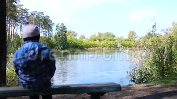 那个孩子坐在公园湖边的一张长凳上在新鲜空气中游走视频的预览图