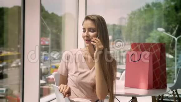年轻漂亮的女孩白天坐在有大窗户的咖啡馆里谈论智能手机城市概念交流视频的预览图