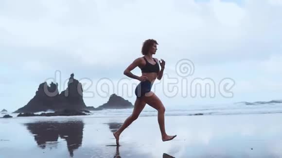 运动女性在海滩上奔跑黑色的沙子在山脉和海洋的背景下缓慢运动加那利视频的预览图