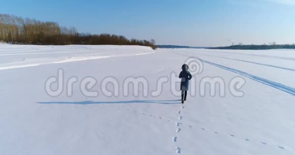 空中镜头奔跑的女人在冬天的风景冻结的河流与森林和城市的景色与视频的预览图