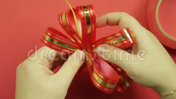 女人双手伸直粉红色丝带礼物蝴蝶结的花瓣给它蝴蝶结的形状红色背景视频的预览图
