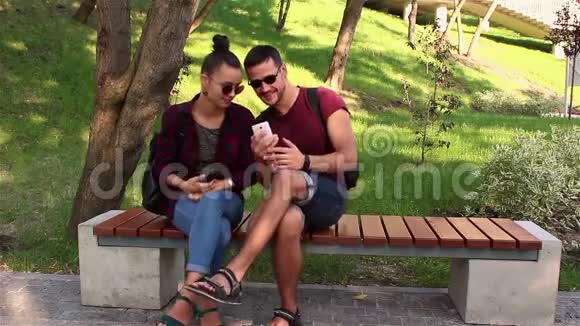 情侣们坐在公园的长椅上在智能手机上展示照片视频的预览图
