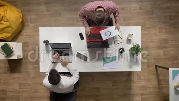年轻笔记本电脑上工作的年轻人把文件交给同事顶头坐在现代办公室的桌子上工作理念视频的预览图