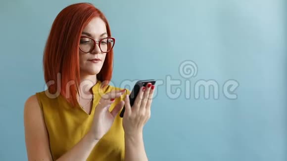 戴眼镜和黄色顶部浏览智能手机的生姜女孩表现出惊喜视频的预览图