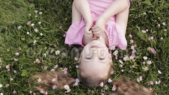 特写微笑的小可爱小女孩躺在绿草上捧着鲜花看着镜头视频的预览图