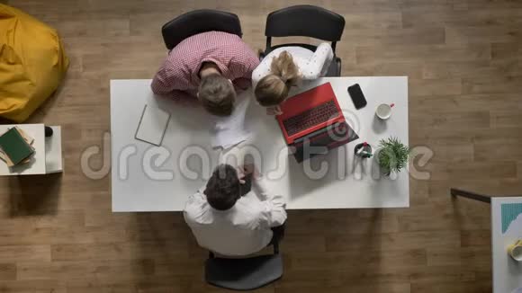 三个年轻的商人团队离开讨论项目顶级人物坐在现代办公室的桌子旁视频的预览图