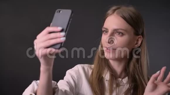 年轻的酷女孩在智能手机上的视频聊天中交流概念灰色背景视频的预览图