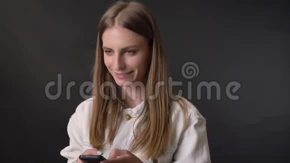 年轻的酷姑娘在智能手机上绑着信息在镜头下观看交流理念灰色背景视频的预览图