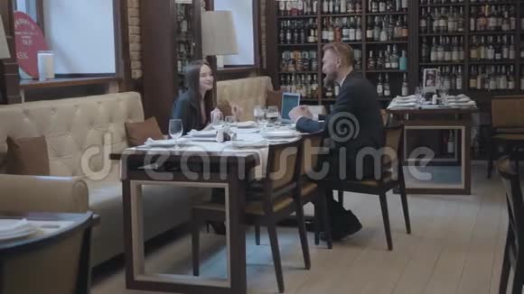 漂亮的黑发女人和金发胡子男人坐在咖啡馆的桌子旁工作笔记本电脑文件和眼镜都打开了视频的预览图