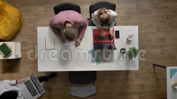 三个年轻人在手提电脑上工作另一个人在办公室写文件顶着头坐在桌子旁打字视频的预览图