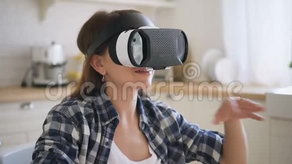 虚拟现实中戴眼镜享受游戏的女人双手和头坐在舒适的厨房里视频的预览图