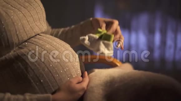 不明身份的孕妇坐在黑暗的房间里的摇椅上玩着一只小袜子踩着它们视频的预览图