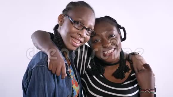 两个年轻漂亮的非洲女人拥抱和笑看着镜头快乐和情感白色工作室背景视频的预览图