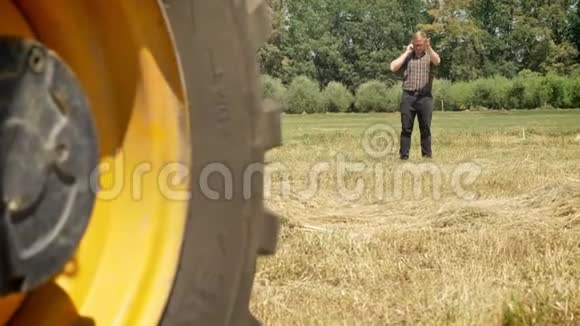 戴眼镜的年轻人打电话走在草田里关心着在拖拉机后面乡下视频的预览图