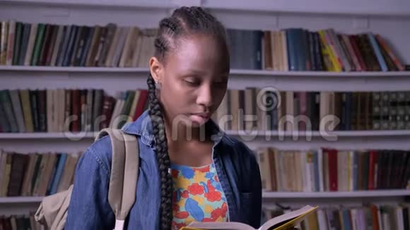 年轻的非裔美国妇女带着背包在图书馆看书看着相机严肃而体贴视频的预览图