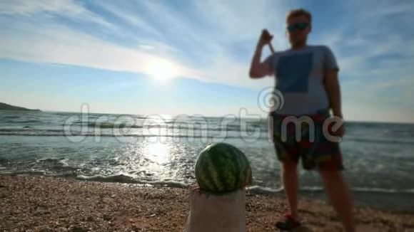 慢动作一个年轻人用蔬菜和西瓜水果敲打棒球棒它位于海滩上视频的预览图