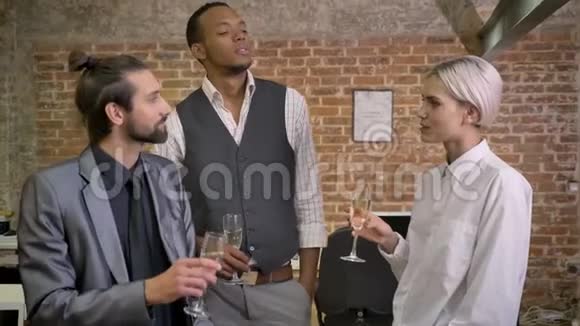 三个不同族裔的工人讲故事开玩笑坐在办公室喝香槟交流观念视频的预览图