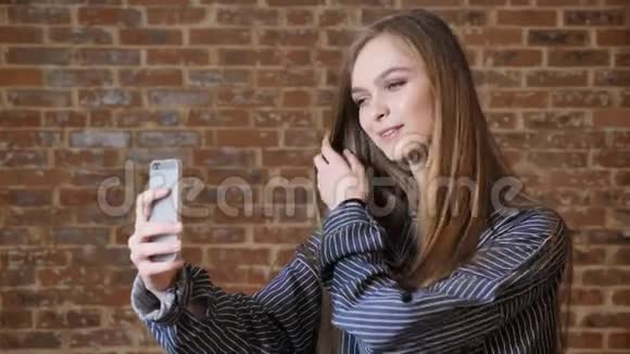 年轻漂亮的女孩正在智能手机上自拍微笑抚摸头发交流理念砖背景视频的预览图