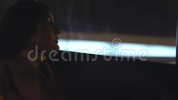 在夜城中行驶的汽车乘客座位上的年轻女子视频的预览图