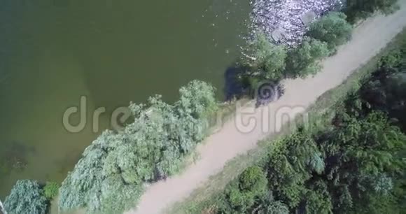 空中无人驾驶飞机俯瞰乡村湖泊有渔夫桥和泥土砾石路视频的预览图
