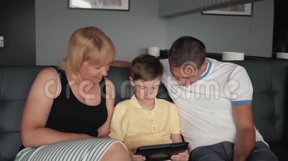 幸福的家庭沙发上有一块平板电脑父母带着一个孩子连接到一个数字平板电脑视频的预览图