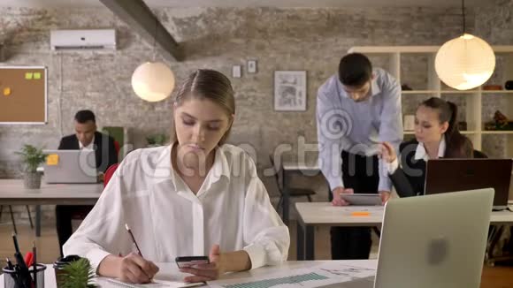 年轻忙碌的女商人正在办公室工作写字手里拿着智能手机讨论背景视频的预览图