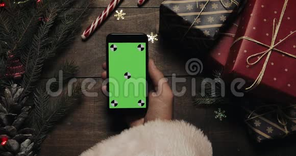 圣诞老人手里拿着绿色屏幕的黑色智能手机铬钥匙上景垂直位置圣诞节视频的预览图