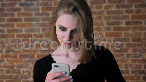 一个眼睛冒烟的年轻女孩正在智能手机上观看照片惊讶交流理念砖背景视频的预览图
