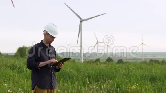 工人站在白色风力涡轮机附近在平板电脑上打字风车绿色能源理念视频的预览图
