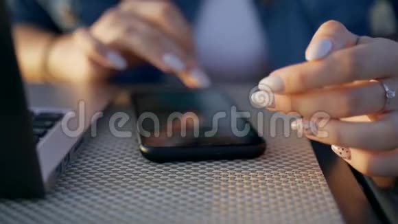 这个女孩正在智能手机上打字一个穿着牛仔夹克的黑发女人坐在一张桌子旁手提电脑和一部智能手机视频的预览图