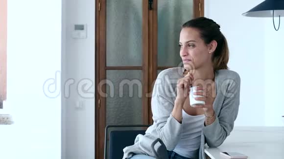漂亮的年轻女人在家坐在厨房里吃酸奶视频的预览图