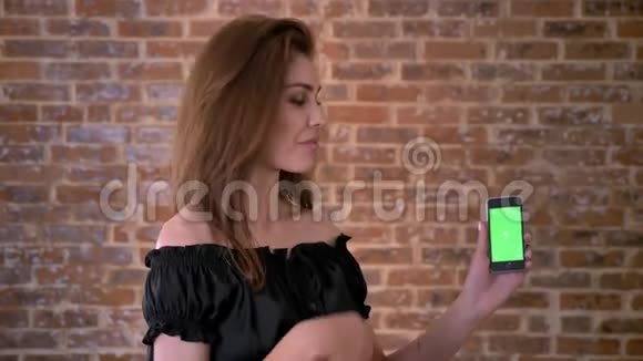 迷人的女人正在展示智能手机的绿色屏幕如标志沟通概念砖背景视频的预览图