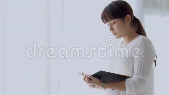 美丽的肖像年轻的亚洲女人站着看书在家里的卧室里考试压力很大视频的预览图