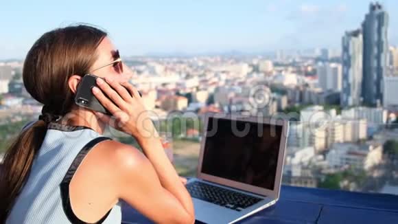 一位女性在屋顶咖啡馆的电脑上工作一边打电话一边观看芭堤雅的全景视频的预览图